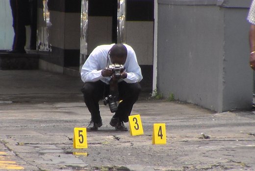 In this June 13, 2013 photo, a police photographer works at the scene where a cop was shot in Kingstown. (IWN photo)