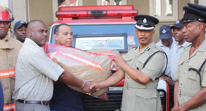 Deputy Commissioner of Police (DCP), Mr.Reynold Hadaway, second from right, receiving a fire suit from Clyde Mofford, a manager at C.K. Greaves & Co.Ltd, left, and Don Carrera, Captain of the Ajax Fire Department, second from left.