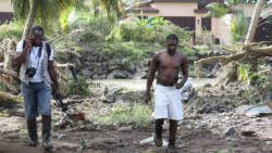 Journalist Kenton X. Chance, left, reports on the impact of the Christmas floods in Buccament Bay. Renrick Quashie, whose house was flooded out, is also pictured. (Photo: Karamo John) 
