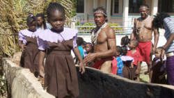 Young students walk through the canoe under construction in Kingstown. 