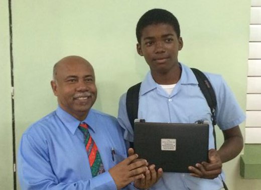 Student Ezra Adams receives a laptop from MP for West St. George, Cecil Ces McKie. (Photo: Camillo Gonsalves/Facebook)