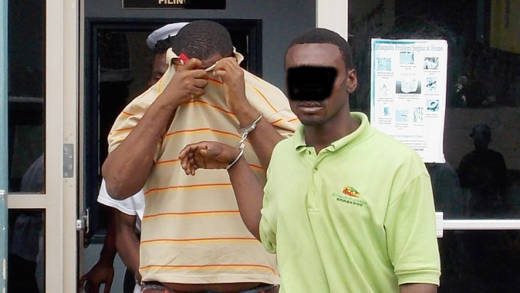 Alister "Tombstone" Smith uses his t-shirt to hide his face as he and another accused man is escorted from court on Monday.