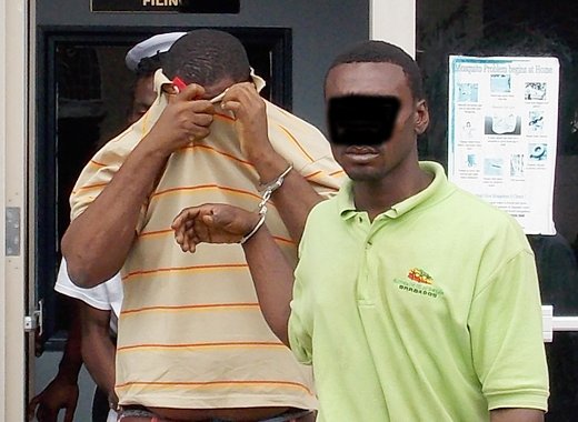 Alister "Tombstone" Smith uses his t-shirt to hide his face as he and another accused man is escorted from court on Monday.
