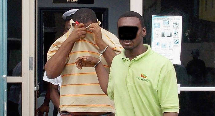 Alister "Tombstone" Smith uses his t-shirt to hide his face as he and another accused man is escorted from court on Monday.