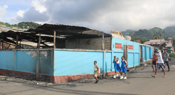 St. Mary's RC student and other pedestrians walk past the burnt out Verbeke Centre on Monday morning. (IWN photo)