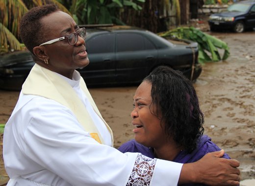 Rev. Eleanor Glasgow prays in Cane Grove on Christmas Day 2013 with Colleen James who lost her sister, Keslia, 18, and 2-year-old daughter Shalarni Headley in the Christmas floods. (IWN photo)