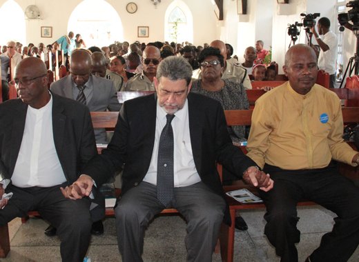 From left: Opposition Leader Arnhim Eustace, Prime Minister Ralph Gonsalves, and Pastor George Frederick join hands during prayer at the memorial service. (IWN photo) 
