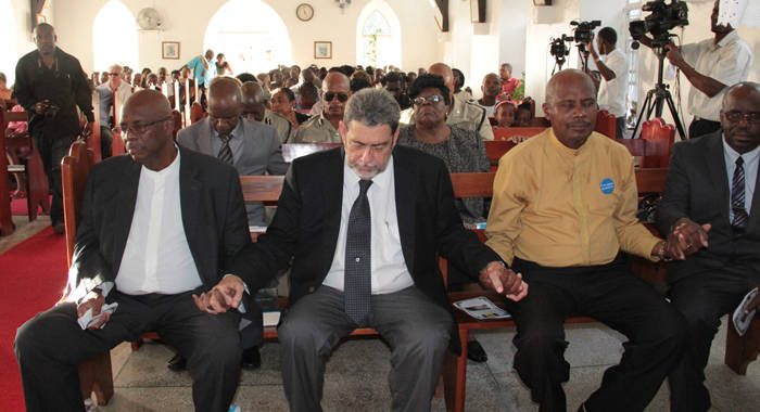 From left: Opposition Leader Arnhim Eustace, Prime Minister Ralph Gonsalves, and Pastor George Frederick join hands during prayer at the memorial service. (IWN photo) 