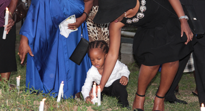 Cane Grove resident Sage Williams on Wednesday is assisted by his mother, Shafia London-Williams as he places a candle in the area where the body of Keslia James was found on Christmas morning 2013. (IWN photo)