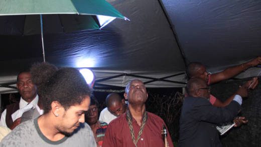 Persons shelter rain under a leaky tent at the Human Rights Association'r prayer and peace rally last weekend. (IWN photo)