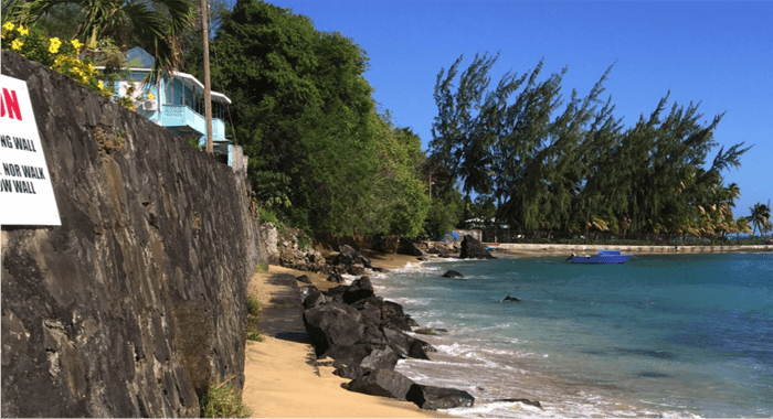 The thin, rock-strewn beachfront at the elite Villa area. The long standing sign warns of the impending collapse of the "defective retaining wall."