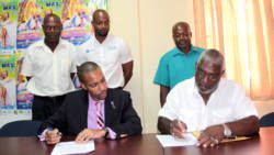 Christopher Gordon of FLOW, left, and Dennis Bowman of CDC, sign the contract while staff of both entities look on. (IWN photo)