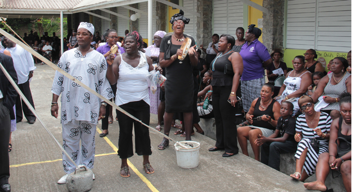 Persons beat tambourines and sing at the funeral in Spring Village on Sunday. (IWN photo)