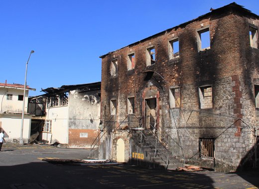 The government will demolish the buildings gutted by fire, including this brick building, left, from the nation's colonial past. (IWN photo)