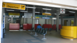 The only occupant (a security guard) in the tiny terminal at Sir James F. Mitchell Airport in front of an out-of-date LIAT sign.