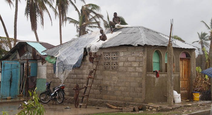 A group of boys makes a desperate attempt on Monday to patch the roof of a house in Les Cayes damaged by Hurricane Matthew. (Photo: CMC/IWN)