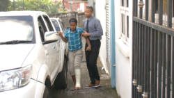 A police officer escorts Baptiste to a police vehicle outside the Serious Offences court on Monday.