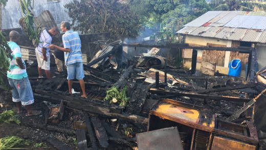 Persons look on at the burnt-out remains of the house on Monday. (iWN photo)
