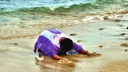 In this undated The Garifuna Heritage Foundation Inc. photo, a Garifuna woman prostrates herself and wails on the sea shore at Balliceaux.