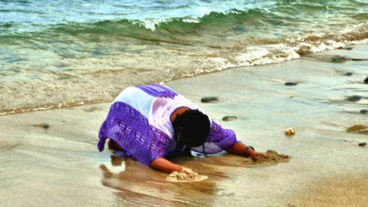 In this undated The Garifuna Heritage Foundation Inc. photo, a Garifuna woman prostrates herself and wails on the sea shore at Balliceaux.