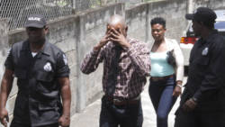Martin James hides his face as police escort him from court after he was freed on a murder charge. He is accompanied by an unidentified woman. (iWN photo)