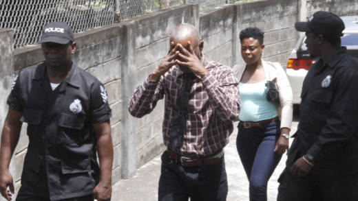 Martin James hides his face as police escort him from court after he was freed on a murder charge. He is accompanied by an unidentified woman. (iWN photo)