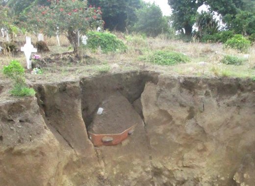 The Sandy Bay cemetery with coffin sticking out of the ground. Tombstones are down and most of the earth is removed.