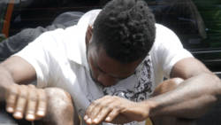 The accused, Mikhail Laidlow, holds down his head so as to avoid being photographed. (iWN photo)