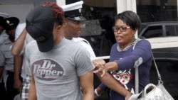 Rosia John, right, seen here in an August 2017 photo as she urged her son, Enrique John, to hide his face after a sex charge, has been charged with murdering one of her son’s relatives, one day after her son was murdered in Kingstown on Friday, April  11, 2026. 