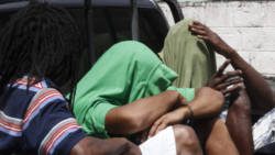 The accused men use their clothing to hide their faces as they are transported to prison. (iWN photo)