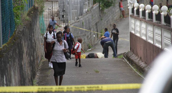 Persons, including students, walk past the body of Michael "Bully" Edwards as police process the scene in Lowmans Hill on Monday. (iWN photo)