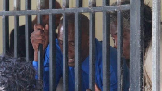 Nigel Morgan, left, and his wife, Althia, speak to their son (not pictured) from inside the holding cell as they await transportation to prison on Monday. (iWN photo)