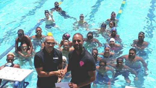 Kyle Dougan, head coach of Black Sands Swim Squad, receives the check from Cedric McIntyre, island manager, Tropical Shipping, as Black Sands Swim Squad swimmers look on.