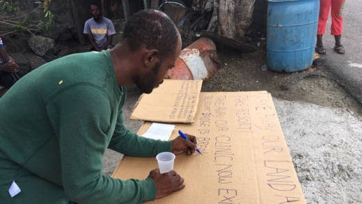 Protestor Cheston Butcher prepares a placard near Buccament Polyclinic on Monday. (iWN photo)