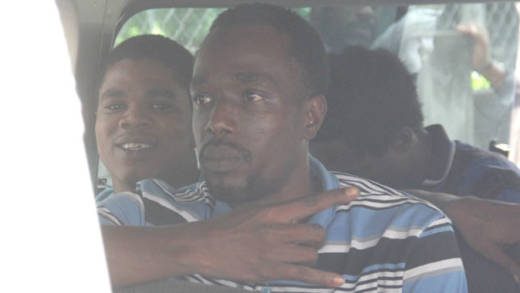Lejah “Soups” Alexander gestures inside a prison van on Friday. At left is accused murderer Jebarry Jackson, who also goes by the name Michael Richards, who had a court appearance in connection with his murder charge. (iWN photo)