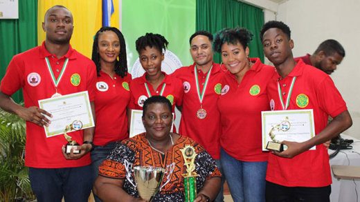  From left, standing: Zachary Richards (debater), Juno Laborde (assistant coach), Haronese Collins (debater), Casey Defreitas (debater), B. Tedra Kirby (coach), and Deaney Gellizeau (debater).  Seated: Eula Adams (SVGCC Deputy Director and local WIDC Chair)