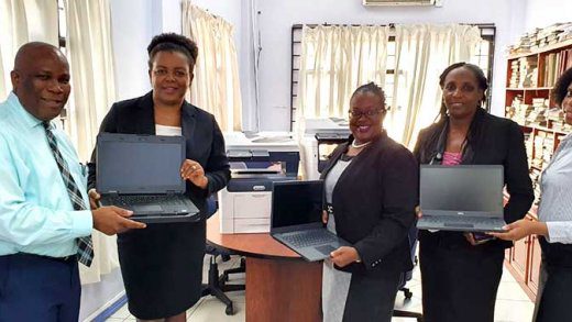 From left: IT Manager, Eastern Caribbean Supreme Court, Mark Ernest presents laptops and printers provided by the UK and US Governments to support remote hearings in the region to Senior Magistrate, Christine Phulchere as Court Administrator, Marlies Agdomar; Senior Executive Officer, Diane Richards, and Supernumerary Clerk, Mykela Samuel display laptops.