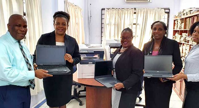 From left: IT Manager, Eastern Caribbean Supreme Court, Mark Ernest presents laptops and printers provided by the UK and US Governments to support remote hearings in the region to Senior Magistrate, Christine Phulchere as Court Administrator, Marlies Agdomar; Senior Executive Officer, Diane Richards, and Supernumerary Clerk, Mykela Samuel display laptops.