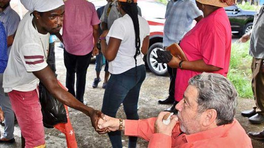 Prime MInister Ralph Gonsalves, right, eats dry coconut and greets a man with dreadlocks during a Sept. 9 visit to Vermont Valley. (Photo: Lance Neverson/Facebook)