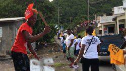 A man donning ULP campaign paraphernalia beats a sheet of metal and mocks NDP supporters as they walk through Sandy on the way to Owia on Sunday. (iWN photo)