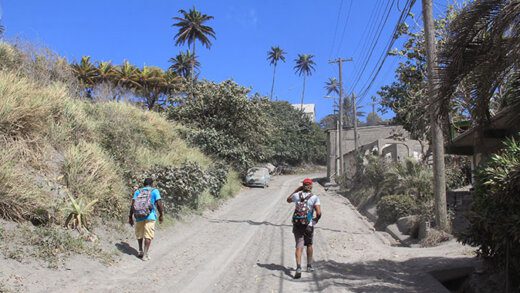 Two men walk along the ash-covered main road in Owia on Thursday. IiWN photo)