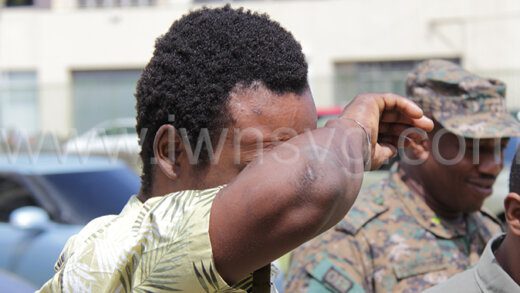 Raphael John uses his hand to hide his face as he is led away to prison on Wednesday, May 17, 2023. 