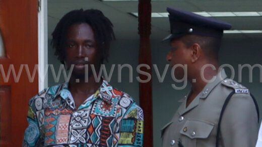 The defendant Esron Cuffy, left, interacts with a police officer outside the Colonarie Magistrate's Court, sitting at Georgetown on Thursday, May 23, 2024.