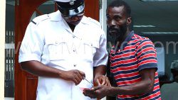 The defendant, Intiad Gordon, left, interacts with a police officer outside the Georgetown Magistrate's Court on March 24, 2025.