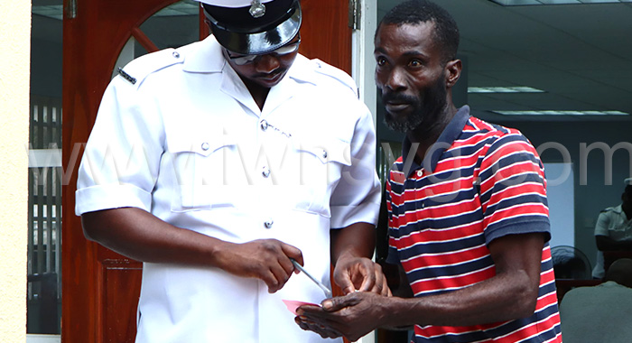 The defendant, Intiad Gordon, left, interacts with a police officer outside the Georgetown Magistrate's Court on March 24, 2025.