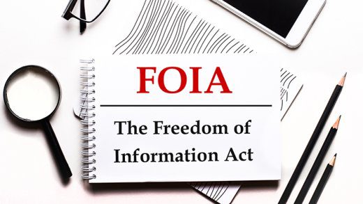 On a white background glasses, a magnifier, pencils, a smartphone and a notebook with the text FOIA The Freedom of Information Act